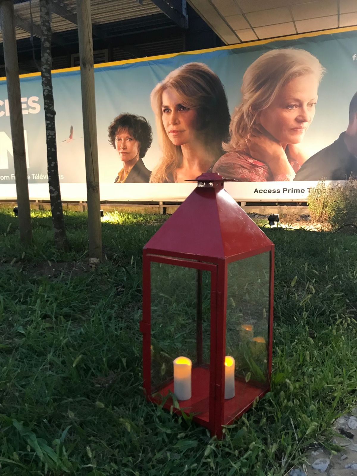 Lanterne rouge avec bougies posée dans l'herbe devant la banderole de la série.